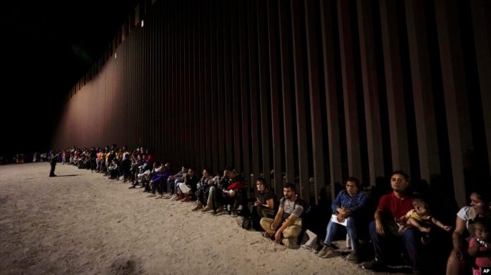 ARCHIVO - Migrantes esperan junto a un muro fronterizo el 23 de agosto de 2022, después de cruzar desde México cerca de Yuma, Arizona.