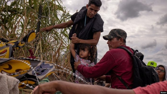Una niña migrante venezolana es asistida por compatriotas mientras intentan pasar entre alambres de púas colocados a lo largo de las orillas del río Grande, en Eagle Pass, EEUU, el 6 de octubre de 2023.